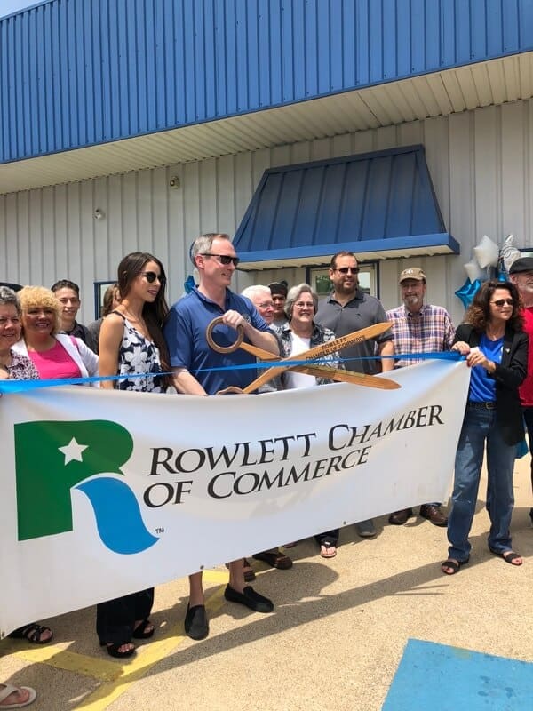 Owner of Accelerate Auto Repair Justin Cole, cuts red ribbon with giant scissors for the Rowlett Tx Chamber of Commerce Grand Opening, with a crowd of loved ones gathered behind him, learn more about Accelerate Auto Repair