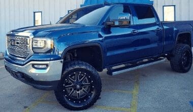 GMC blue lifted pickup truck that came in for collision work parked sideways in front of Accelerate Auto Repair in Rowlett Tx